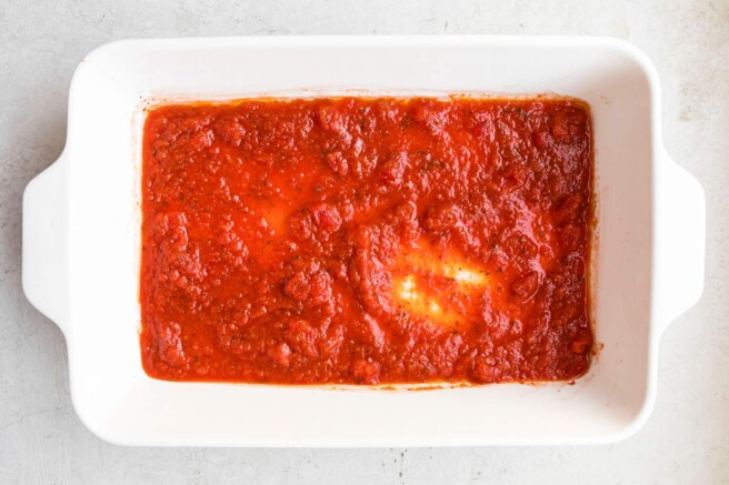 Tomato sauce evenly spread in the bottom of a casserole dish.