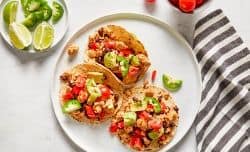 turkey tacos served in corn tortillas and topped with diced tomato, avocado and jalapeños