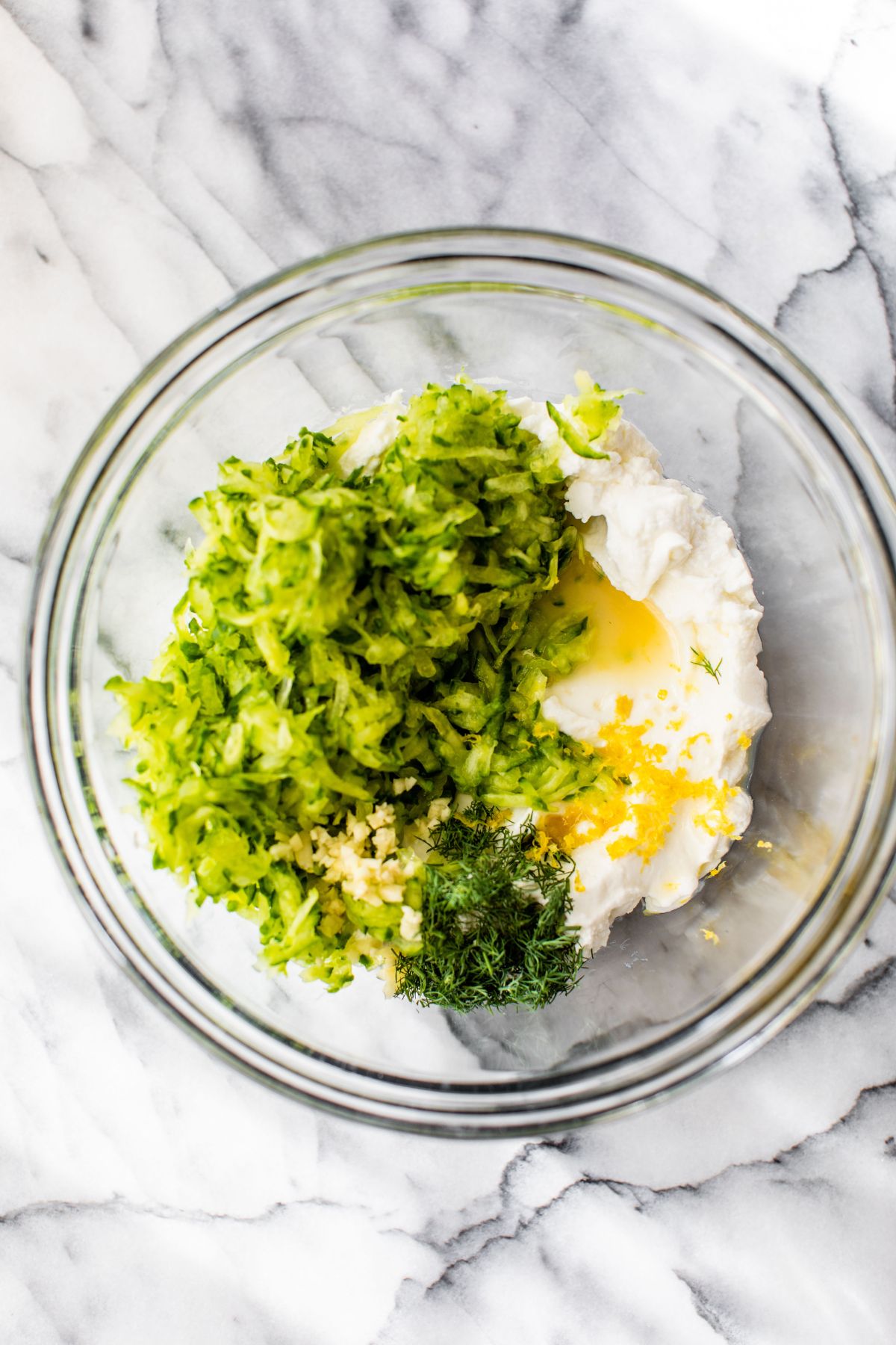 Combining ingredients in a medium bowl for tzatziki sauce.